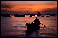 Man in a small boat, with moored boats seen against a vivid sunset. Vung Tau, Vietnam (color)