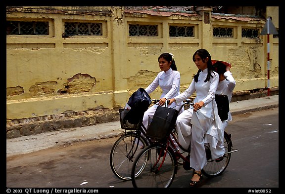 Senior high school girls ride bicycles with impeccable style, wearing elegant Ao Dai uniforms. Ho Chi Minh City, Vietnam (color)