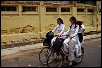 Senior high school girls ride bicycles with impeccable style, wearing elegant Ao Dai uniforms. Ho Chi Minh City, Vietnam